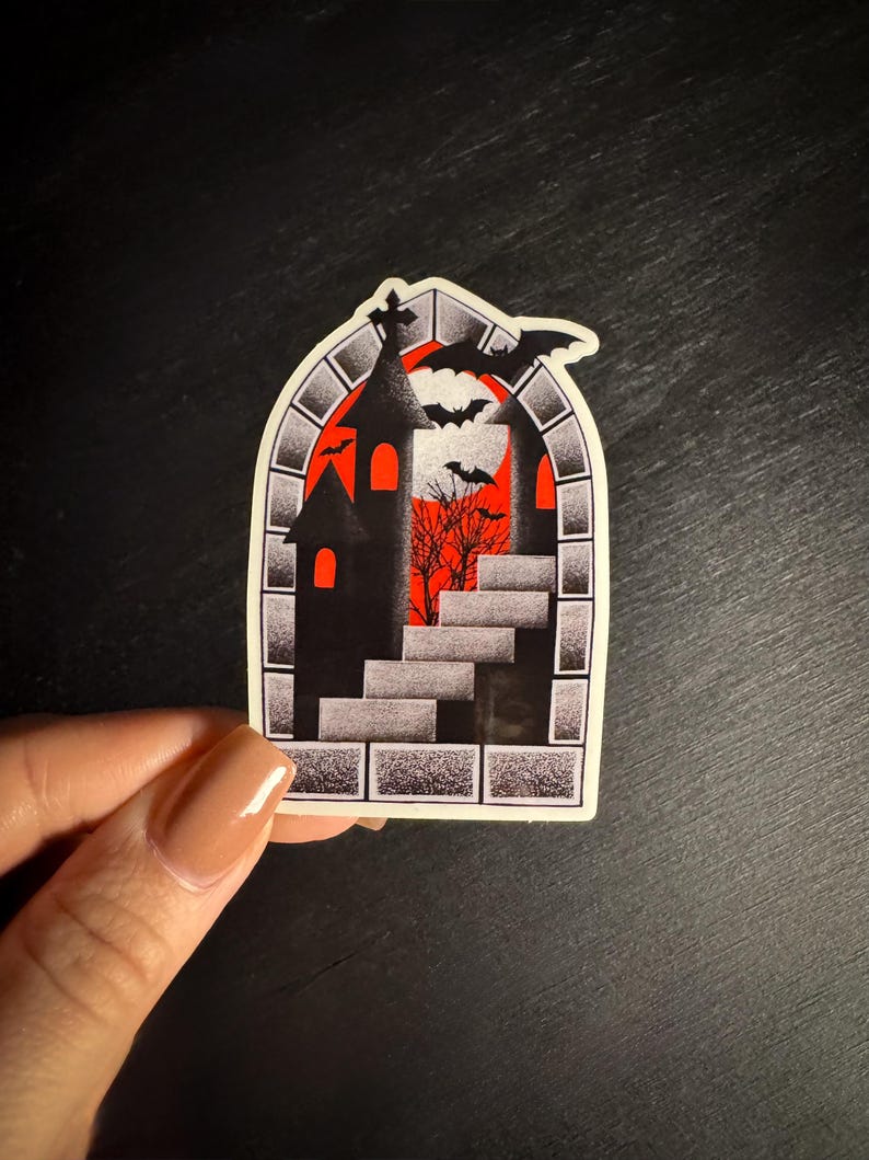 Puede incluir: Una pegatina de Halloween con una silueta de castillo negro, murci&eacute;lagos y una escalera sobre un fondo rojo y naranja. El dise&ntilde;o est&aacute; enmarcado por un borde de piedra. La pegatina est&aacute; sujeta por una mano.