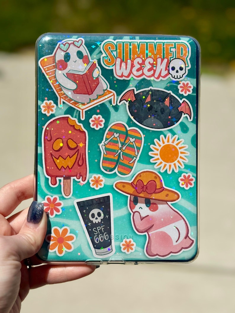 May include: A clear phone case decorated with summer-themed stickers. The stickers include a ghost reading a book, a bat, a popsicle, flip-flops, a sun, and a tube of SPF 666 sunscreen. The words "SUMMER WEEK" are also visible.