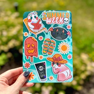 May include: A teal sticker sheet with various summer-themed illustrations. Includes a ghost reading a book, a bat, a popsicle, flip-flops, a sun, a ghost wearing a hat, and a tube of SPF 666. The words "SUMMER WEEK" are also present.