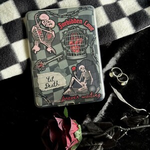 Op de afbeelding: Een doorzichtige telefoonhoes met een gothic thema, met illustraties van skeletten, kettingen en de zinnen "Forbidden Love", "Til Death" en "forever waiting". Een rode roos en zilveren ringen zijn ook zichtbaar.