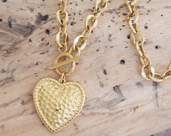 Collar de cadena gruesa de acero dorado con colgante de corazón martillado. Cierre en T. Collar con cierre de palanca. Regalo de San Valentín.