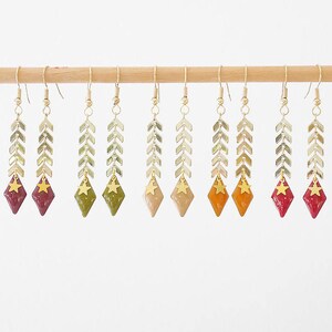 Peut inclure: Huit paires de boucles d'oreilles dorées avec un charme en forme d'étoile et une chaîne pendante de perles en forme de flèche. Les boucles d'oreilles sont dans des tons de rouge, orange et vert.
