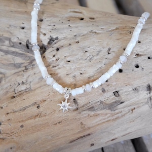 May include: A white beaded bracelet with a silver star charm. The beads are small and round, and the star charm has a small clear stone in the center.