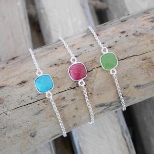 May include: Three silver chain bracelets with square-shaped gemstone charms. The charms are turquoise, red, and green.