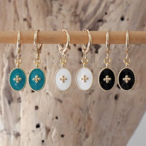 Puede incluir: Seis pendientes de aro dorados con colgantes ovalados de borde perlado. Los colgantes están rellenos de esmalte en color verde azulado, blanco y negro, cada uno con un pequeño motivo floral dorado de cuatro pétalos en el centro.