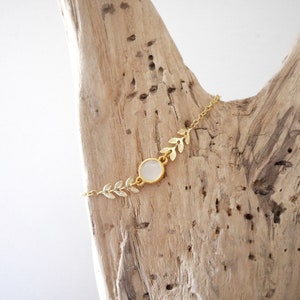 Op de afbeelding: Een delicate gouden kettingarmband met een witte edelsteen en bladeren accenten.
