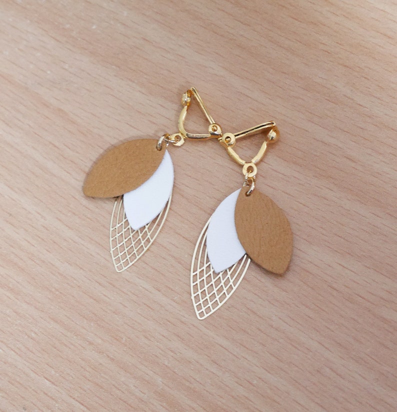 May include: A pair of gold tone clip-on earrings with a layered design. The earrings feature two brown and white leaf shapes with a gold wire mesh pattern.