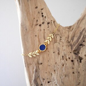 Op de afbeelding: Gouden kettingarmband met een blauwe edelsteen en blaadjesvormige bedels.