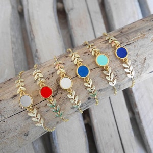 Op de afbeelding: Vijf gouden bladeren armbanden met verschillende gekleurde emaille cirkels. De cirkels zijn rood, wit, turquoise, donkerblauw en lichtblauw.