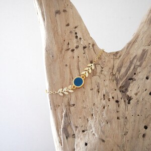 Op de afbeelding: Een gouden kettingarmband met een blauwe ronde bedel en gouden bladeren accenten.