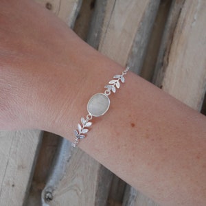 Puede incluir: Una pulsera de plata con una piedra ovalada blanca y un dise&ntilde;o de hojas.