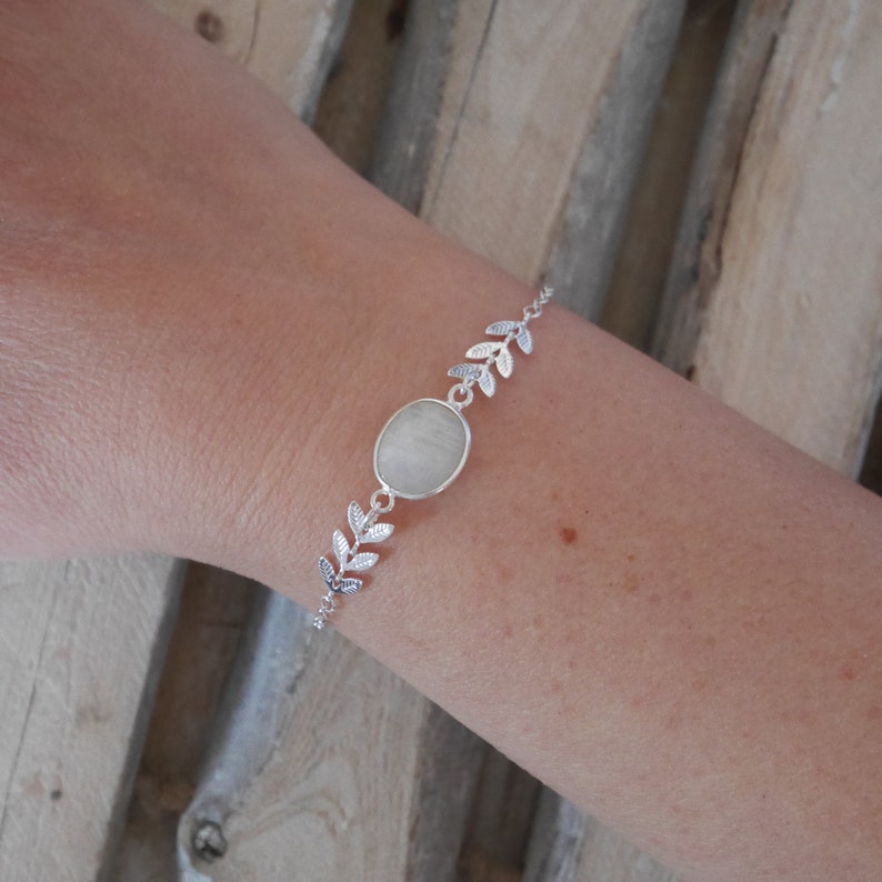 Puede incluir: Una pulsera de plata con una piedra ovalada blanca y un dise&ntilde;o de hojas.