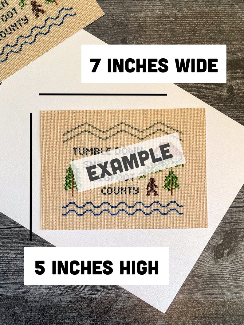 May include: A beige cross-stitch pattern with a brown bear, green trees, and blue waves. The pattern says "Tumble Down Sugar Creek County". The pattern is 7 inches wide and 5 inches high.