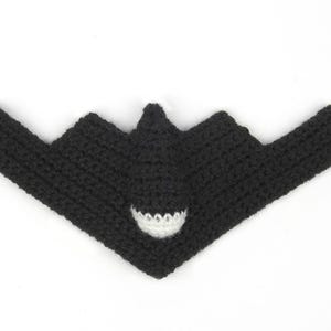 May include: A black crocheted B-2 bomber airplane with a white accent. The handmade airplane has a distinctive wing shape and a detailed cockpit area. The craft is displayed on a white background.