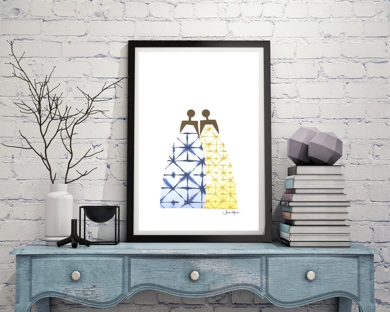 May include: A framed print of two figures in blue and yellow patterned dresses, standing back to back. The print is on a white background and has the artist's signature in the bottom right corner.