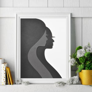 May include: A black and white framed print of two abstract faces in profile, with the faces overlapping. The print is hanging on a white wall with a white wainscoting design.