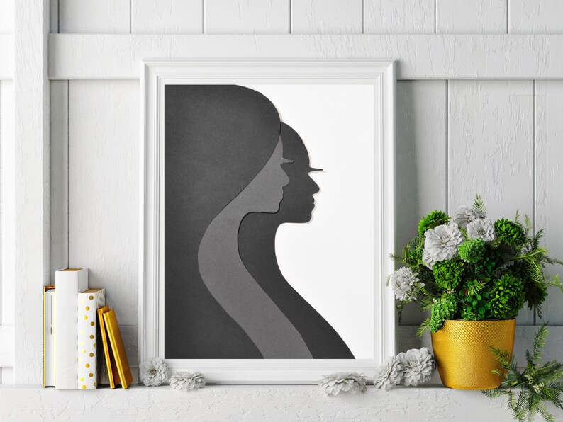 May include: A black and white framed print of two abstract faces in profile, with the faces overlapping. The print is hanging on a white wall with a white wainscoting design.