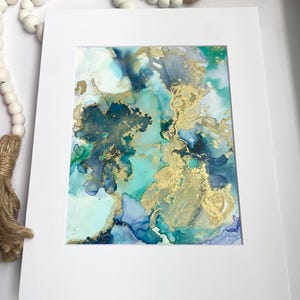 May include: Abstract painting with blue, green, and gold colors. The painting is framed in a white mat.