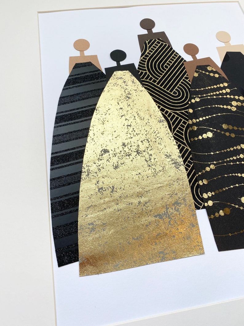 May include: A framed art piece featuring five figures with black, gold, and brown paper cutouts. The figures are wearing different patterned dresses, including stripes, geometric designs, and polka dots.