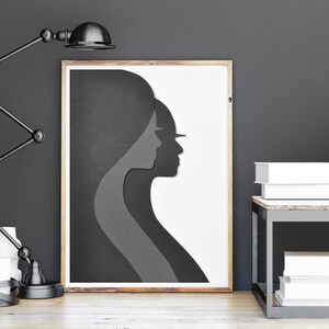 May include: A black and white framed print of a layered silhouette of two people's faces. The print is on a white background and is hanging on a grey wall.