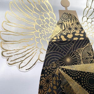 May include: A gold and black paper angel with geometric patterns against a white background.