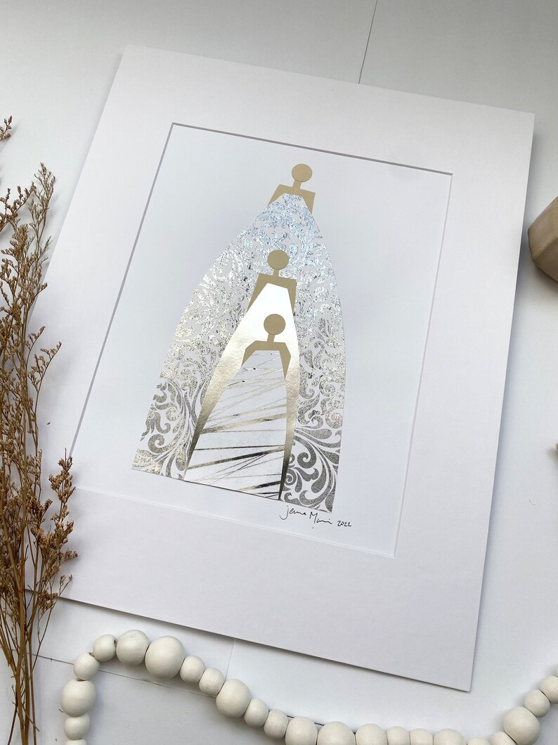 May include: A white matted print with a gold silhouette of three figures standing on top of each other. The figures are surrounded by a silver patterned background. The print is signed "Jenna Mani 2022" in the bottom right corner.