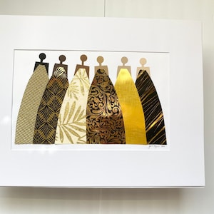 May include: A framed collage of seven figures in a row, each wearing a different gold patterned dress. The dresses are made of various materials, including metallic paper, fabric, and foil. The figures are all the same size and shape, and they are arranged in a symmetrical pattern.
