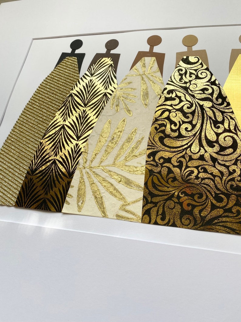 May include: A framed art print featuring five figures in a row, each wearing a different gold patterned dress. The dresses are made of various textures and patterns, including stripes, leaves, and swirls.