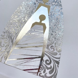 May include: A silver and gold abstract art print with a stylized image of two figures. The print has a silver background with a gold floral pattern. The artist's signature "Jena Mani 2022" is in the bottom right corner.