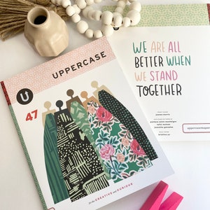 May include: A magazine cover with the title "UPPERCASE" and the number 47. The cover features a colourful illustration of people standing together. The text "WE ARE ALL BETTER WHEN WE STAND TOGETHER" is printed on the cover.