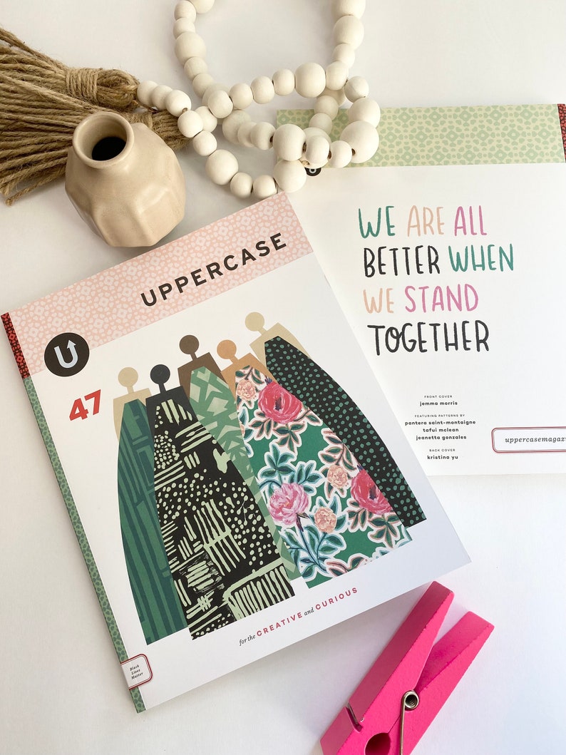 May include: A magazine cover with the title "UPPERCASE" and the number 47. The cover features a colourful illustration of people standing together. The text "WE ARE ALL BETTER WHEN WE STAND TOGETHER" is printed on the cover.
