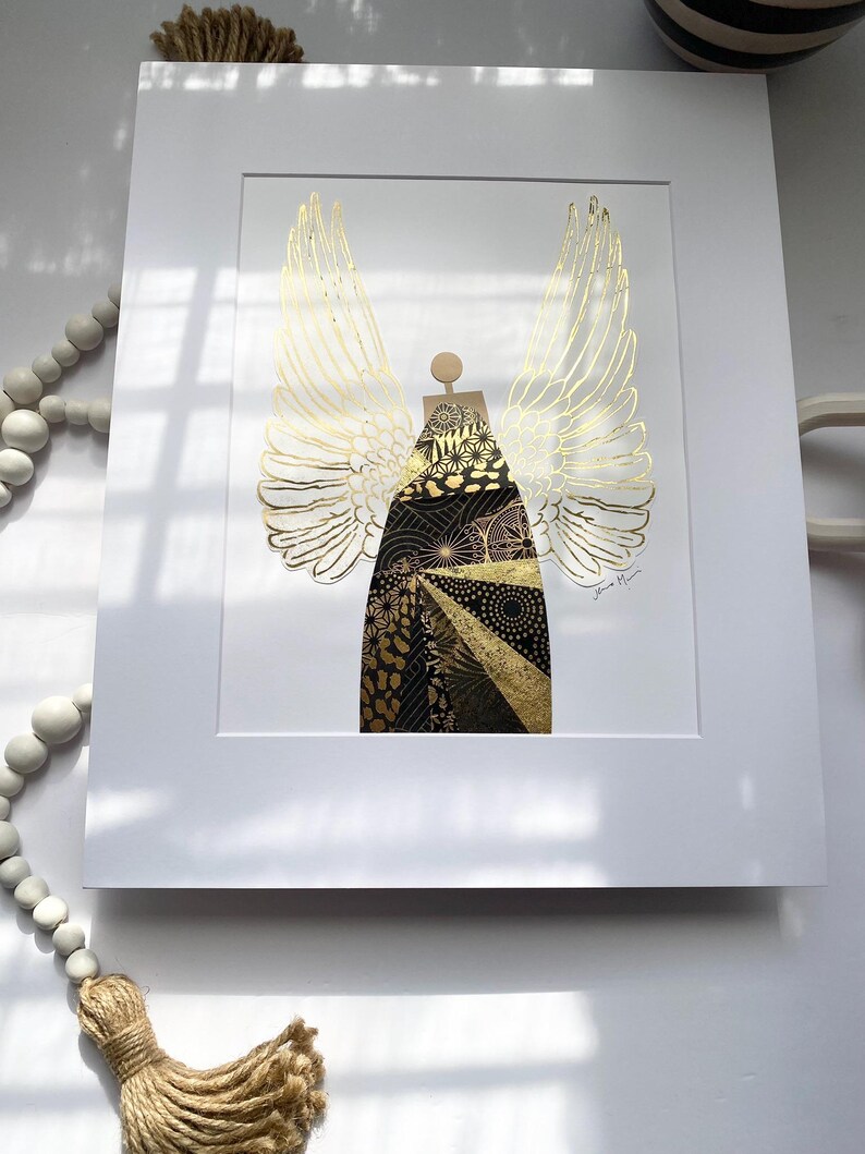May include: A gold and black angel with wings made of gold foil. The angel is standing on a white background. The artist's signature is in the bottom right corner.