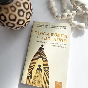 May include: A book titled "Black Women and Da 'Rona: Community, Consciousness, and Ethics of Care" edited by Julia S. Jordan-Zachery and Shamara Wyllie Alhassan. The cover features a stylised black and gold illustration of a woman standing inside a doorway.