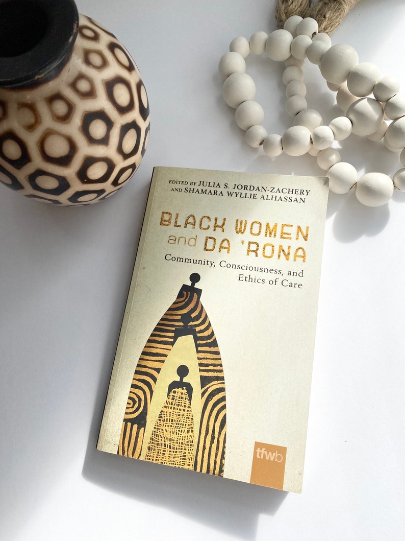 May include: A book titled "Black Women and Da 'Rona: Community, Consciousness, and Ethics of Care" edited by Julia S. Jordan-Zachery and Shamara Wyllie Alhassan. The cover features a stylised black and gold illustration of a woman standing inside a doorway.