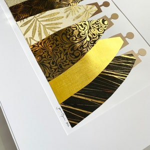 May include: A framed art print featuring a collage of gold and black patterned paper cut into the shape of stylized figures. The print is signed "Jenna Mari - 2022".