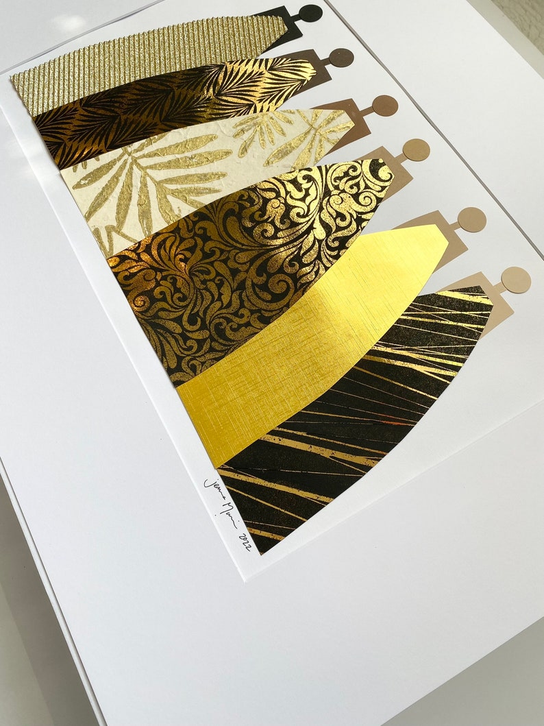 May include: A framed art print featuring a collage of gold and black patterned paper cut into the shape of stylized figures. The print is signed "Jenna Mari - 2022".