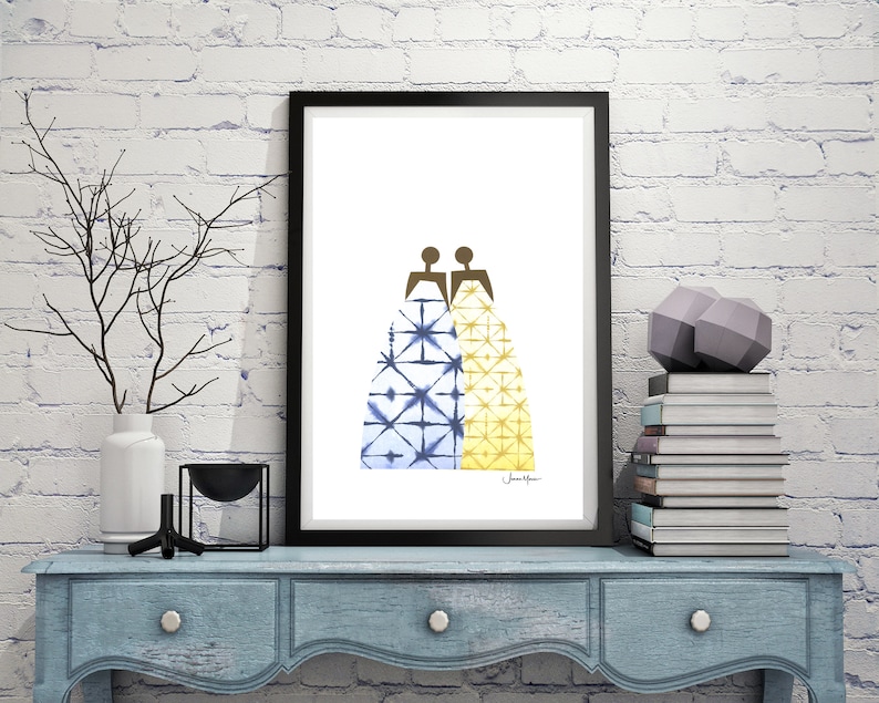 May include: A framed print of two figures in blue and yellow patterned dresses, standing back to back. The print is on a white background and has the artist's signature in the bottom right corner.