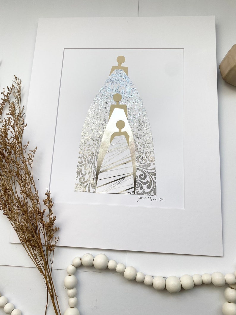 May include: A white matted print of a gold and silver abstract art piece depicting three figures standing on top of each other. The figures are outlined in gold and the background is a silver patterned design. The artist's signature and the year 2021 are in the bottom right corner of the print.