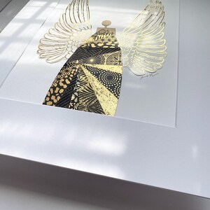 May include: A black and gold geometric angel with wings, framed in white. The artist's signature is visible in the bottom right corner.