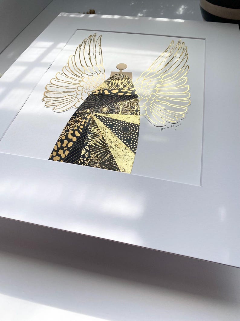 May include: A black and gold geometric angel with wings, framed in white. The artist's signature is visible in the bottom right corner.