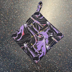 May include: A black and purple pot holder with a repeating pattern of the Evil Queen from Snow White. The pot holder has a loop handle.