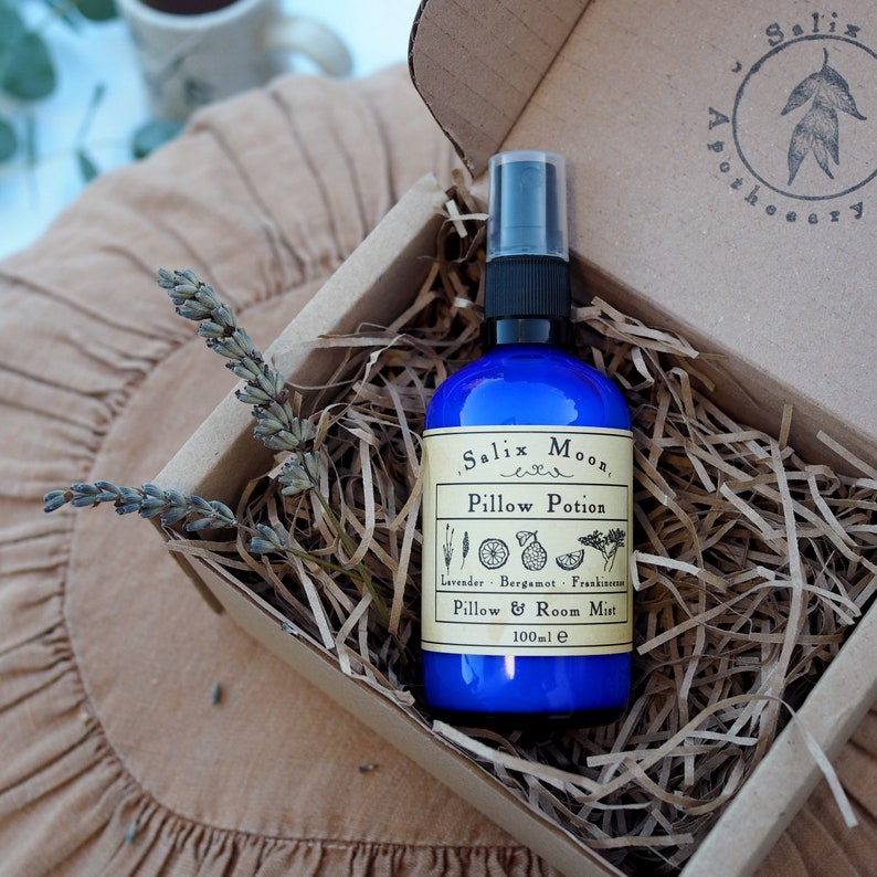 May include: A blue glass bottle with a spray nozzle, labeled "Salix Moon Pillow Potion", containing a lavender, bergamot, and frankincense pillow and room mist. The bottle is in a brown cardboard box with shredded paper.