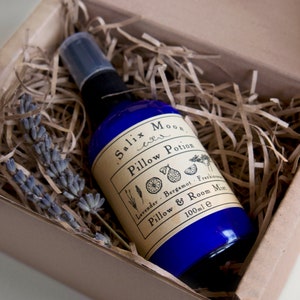 May include: A blue glass bottle with a spray nozzle, filled with a clear liquid. The bottle has a label that reads "Salix Moon Pillow Potion Lavender - Bergamot - Frankincense Pillow & Room Mist 100ml e".