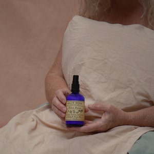 May include: A blue glass bottle with a black spray nozzle and a brown label that reads "Salix Moon Apothecary Pillow Potion Lavender, Bergamot, Frankincense, Ylang Ylang, Rose Marigold 100ml e"