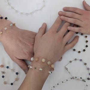 Könnte beinhalten: Eine Sammlung handgefertigter, drahtgewickelter Armbänder mit verschiedenen farbigen Edelsteinen. Die Armbänder haben unterschiedliche Farben und Muster, darunter Blau, Grün, Braun und Weiß.