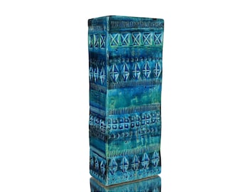 Könnte beinhalten: Eine hohe, rechteckige Keramikvase mit einer leuchtend blauen und türkisfarbenen Glasur. Die Oberfläche ist mit horizontalen Bändern aus geprägten geometrischen Mustern verziert, darunter Reihen von Rauten, Quadraten und vertikalen Linien.