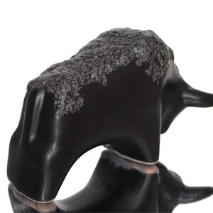May include: Black ceramic bull figurine with a textured surface. The bull is standing on its four legs with its head turned to the side.