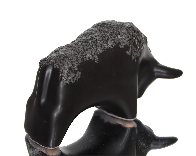 May include: Black ceramic bull figurine with a textured surface. The bull is standing on its four legs with its head turned to the side.