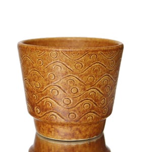 Könnte beinhalten: Ein brauner Keramiktopf mit einem wellenförmigen Muster. Der Topf hat eine breite Öffnung und einen schmalen Boden.