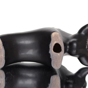 May include: Black ceramic bull figurine with a hole in the bottom. The figurine is lying on its side.